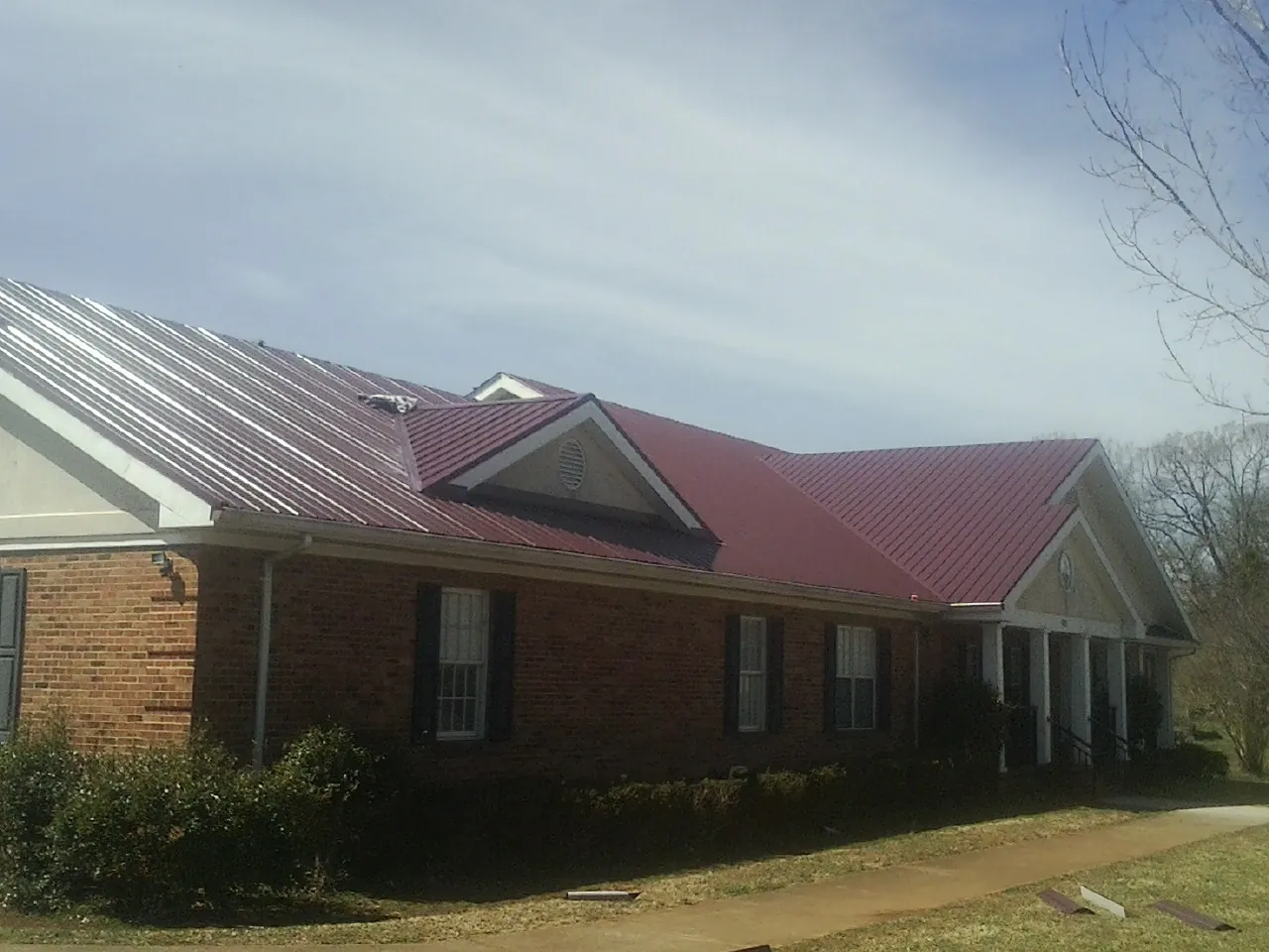 Red metal roof with gabled entries on a long brick building, from a Hail Damage Roof Repair job in Dewitt