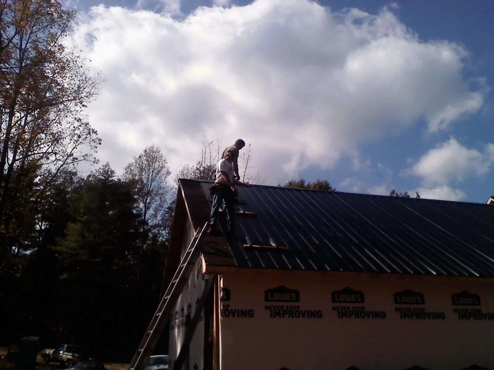 Roofer fastening dark metal panels high against a cloudy sky, from a Roof Inspection job in Dewitt